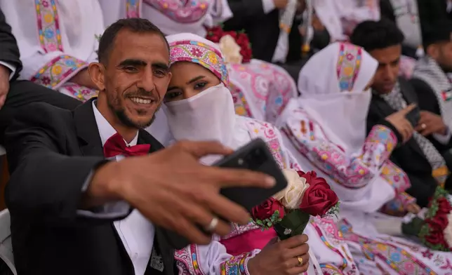 A Palestinian couple poses for a selfie as they get married in a mass wedding ceremony in Deir al-Balah, central Gaza Strip, Friday, April 24, 2026. (AP Photo/Abdel Kareem Hana)