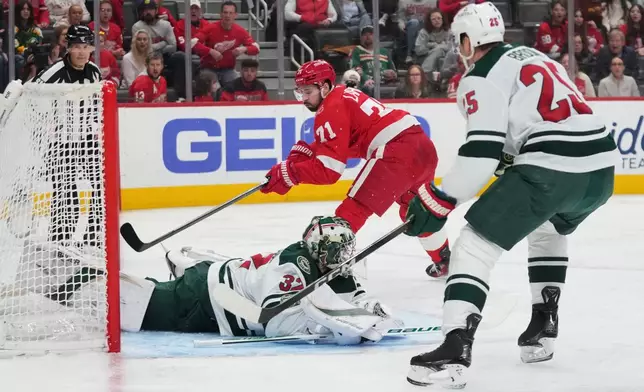 Detroit Red Wings center Dylan Larkin (71) shoots but misses as Minnesota Wild goaltender Filip Gustavsson (32) defends and defenseman Jonas Brodin (25) looks on in the second period of an NHL hockey game Sunday, April 5, 2026, in Detroit. (AP Photo/Paul Sancya)