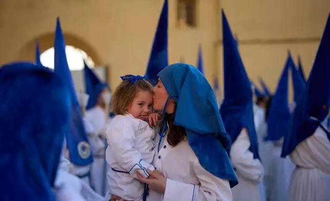 A hooded penitent of the Nuestro Padre Jesus Cautivo y Nuestra Senora de la Estrella brotherhood kisses her child during a Holy Week procession in Dona Mencia, southern Spain, Tuesday, March 31, 2026. (AP Photo/Manu Fernandez)