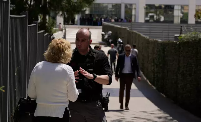 A policeman speaks with a woman outside a courthouse after a gunman opened fire leaving several people wounded in Athens, Tuesday, April 28, 2026. (AP Photo/Petros Giannakouris)