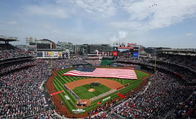 An American flag is held across the field during the national anthem as F-16C Fighting Falcons flyover before the Washington Nationals home-opener baseball game against the Los Angeles Dodgers, Friday, April 3, 2026, in Washington. (AP Photo/Terrance Williams)