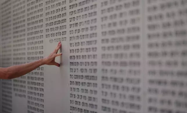 A man touches the wall with names of fallen soldiers during Israel's annual Memorial Day for the soldiers who died in the nation's conflicts and victims of nationalistic attacks at the Armored Corps memorial site in Latrun, Israel, Tuesday, April 21, 2026. (AP Photo/Ariel Schalit)