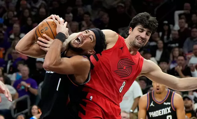 Phoenix Suns guard Devin Booker (1) gets fouled by Portland Trail Blazers forward Deni Avdija (8) during the second half of an NBA play-in tournament basketball game, Tuesday, April 14, 2026, in Phoenix. (AP Photo/Ross D. Franklin)
