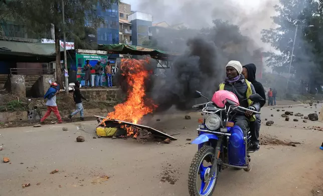 People ride past burning tyres during a public transport strike over fuel prices in Nairobi, Kenya, Monday, May 18, 2026. (AP Photo/Andrew Kasuku)
