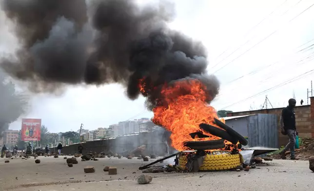 A man walks past burning tyres during a public transport strike over fuel prices in Nairobi, Kenya, Monday, May 18, 2026. (AP Photo/Andrew Kasuku)