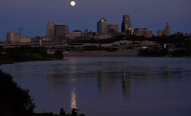 FILE - People fish in the Kansas River as the full moon rises beyond the downtown skyline, May 11, 2025, in Kansas City, Mo. (AP Photo/Charlie Riedel, file)