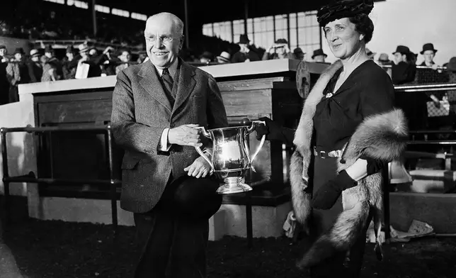 FILE- Samuel Riddle, left, owner of War Admiral, is presented with the trophy by Dorothy Butler wife of track owner James Butler Jr., after War Admiral won the Washington handicap horse race at Laurel Park, Md., Oct. 30, 1937. (AP Photo/Henry Griffin, File)