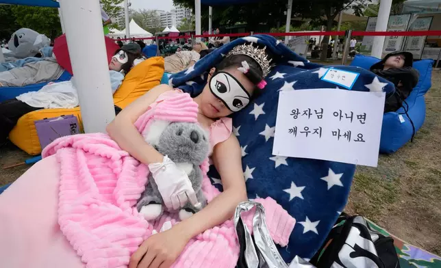 A participant takes a nap during the 2026 Hangang Nap Competition at Yeouido Hangang Park in Seoul, South Korea, Saturday, May 2, 2026. The writing reads "Don't wake me up unless it's a prince." (AP Photo/Ahn Young-joon)
