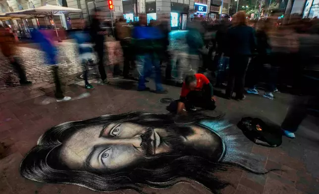 FILE - Street artist Mauro Maureira paints an image of Jesus Christ as faithful take part in the Christ of May procession in Santiago, Chile, May 13, 2026. (AP Photo/Esteban Felix, File)
