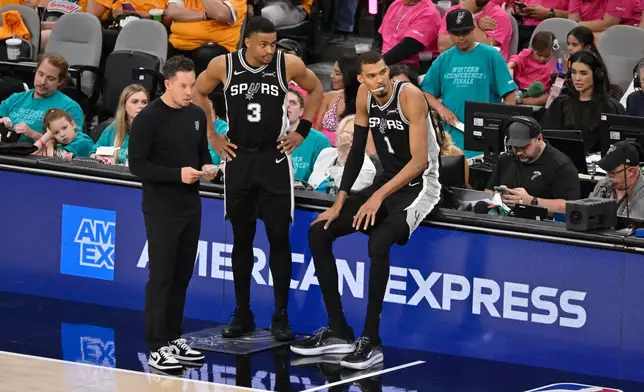 San Antonio Spurs head coach Mitch Johnson, forwards Keldon Johnson (3) and Victor Wembanyama (1) look on during the second half of Game 3 in the Western Conference finals NBA basketball playoffs series against the Oklahoma City Thunder Friday, May 22, 2026, in San Antonio. (AP Photo/Darren Abate)