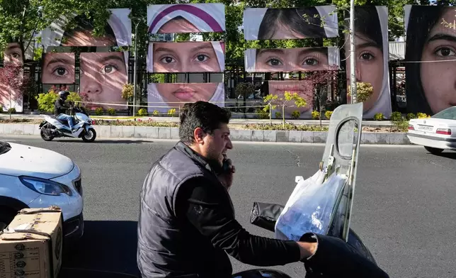 Vehicles drive past banners showing portraits of the school children who were killed during a strike on a school in southern town of Minab on Feb. 28, at Tajrish square in northern Tehran, Iran, Sunday, May 10, 2026. (AP Photo/Vahid Salemi)