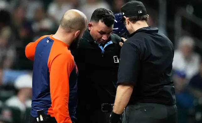 Umpire Roberto Ortiz, center, is checked out for injury before leaving the game during the sixth inning of a baseball game between the Seattle Mariners and the Houston Astros in Houston, Wednesday, May 13, 2026. (AP Photo/Ashley Landis)
