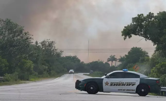 A Broward County Sheriff's police car blocks the entrance to a park as a wildlife burns in Broward County, Fla., Monday, May 11, 2026. (AP Photo/Marta Lavandier)