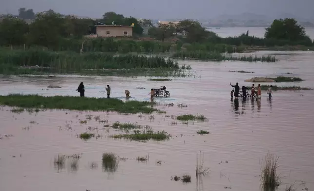 Residents wade through floodwaters along the banks of the Euphrates River near Raqqa, northeastern Syria, Tuesday, May 26, 2026. (AP Photo/Baderkhan Ahmad)