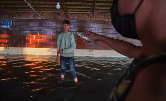 A man holds a fish caught while inspecting a flooded restaurant along the banks of the Euphrates River near Raqqa, northeastern Syria, Tuesday, May 26, 2026. (AP Photo/Baderkhan Ahmad)