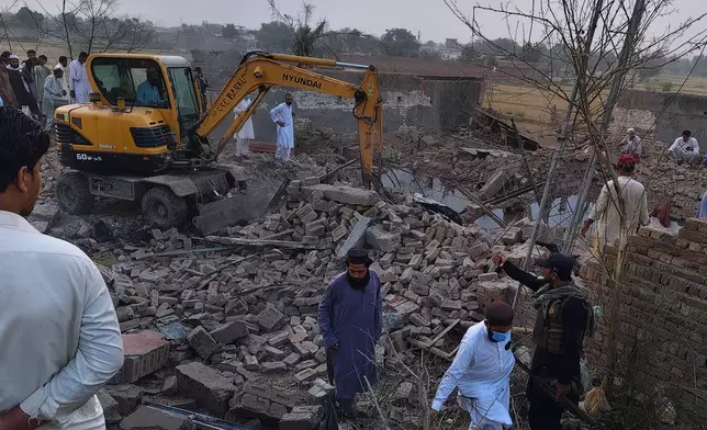 A worker clear rubble with an excavator as a police officer and local residents gather at the site of overnight suicide bombing at a security post in Fatah Khel, in Bannu, a district in Pakistan's Khyber Pakhtunkhwa province bordering Afghanistan, Sunday, May 10, 2026. (AP Photo/Aamad Khattak)