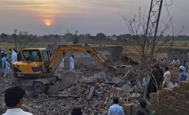 A worker clear rubble with an excavator as a police officers and local residents gather at the site of overnight suicide bombing at a security post in Fatah Khel, in Bannu, a district in Pakistan's Khyber Pakhtunkhwa province bordering Afghanistan, Sunday, May 10, 2026. (AP Photo/Aamad Khattak)