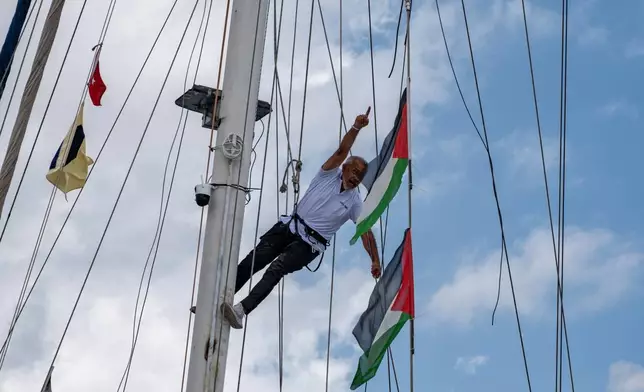 An activist chants slogans while hanging Palestinian flags on a boat belonging to the Global Sumud Flotilla, carrying activists and humanitarian aid, as it prepares to depart for Gaza from the port of Marmaris, Turkey, Thursday, May 14, 2026, in an attempt to break the Israeli naval blockade. (AP Photo/Murat Kocabas)