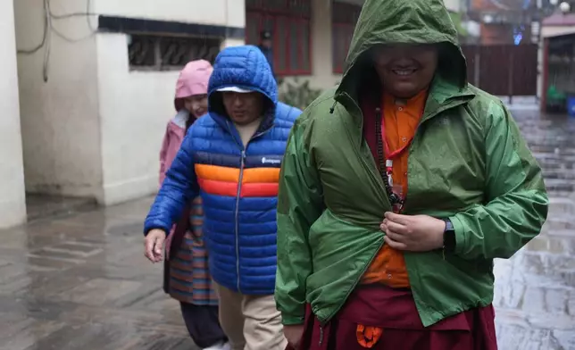 U.S.-born Buddhist lama Jalue Dorje walks in the rain with his parents, Dorje Tsegyal and Dechen Wangmo, during a 12-day series of rituals and teachings at Shechen Monastery in Kathmandu, Nepal, on Wednesday, April 8, 2026. (AP Photo/Luis Andres Henao)