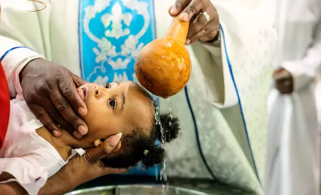 A priest pours water over the head of a child during a baptism ceremony at the Roman Catholic Cathedral in Harare, Zimbabwe, Sunday, April 5, 2026. (AP Photo/Aaron Ufumeli)