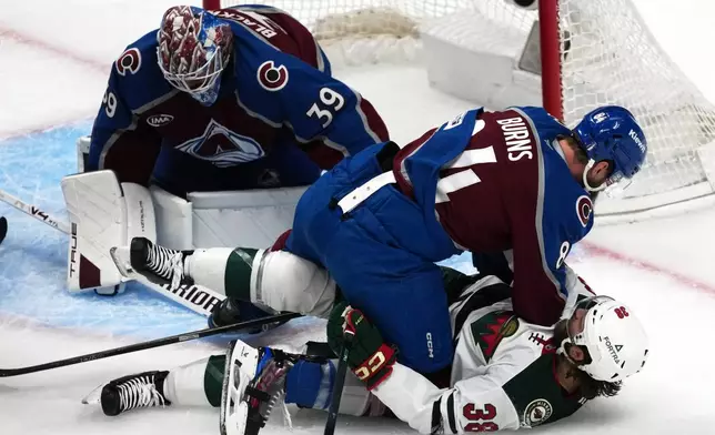 Colorado Avalanche defenseman Brent Burns, top front, pins Minnesota Wild right wing Ryan Hartman as Colorado goaltender MacKenzie Blackwood looks on in the first period of Game 5 of an NHL Stanley Cup hockey second-round playoff series, Wednesday, May 13, 2026, in Denver. (AP Photo/David Zalubowski)