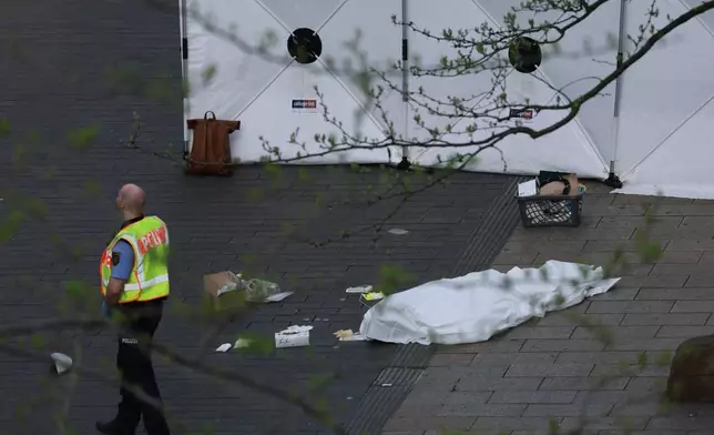 A policeman stands next to a body bag after a car crashed into several people in Leipzig, Germany, Monday, May 4, 2026. (Jan Woitas/dpa via AP)