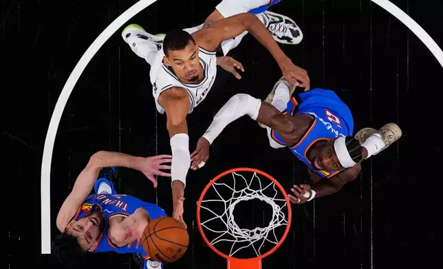 San Antonio Spurs forward Victor Wembanyama (1) drives to the basket against Oklahoma City Thunder center Chet Holmgren (7) and guard Shai Gilgeous-Alexander (2) during the first half in Game 4 in the Western Conference finals NBA basketball playoffs series in San Antonio, Sunday, May 24, 2026. (AP Photo/Eric Gay)