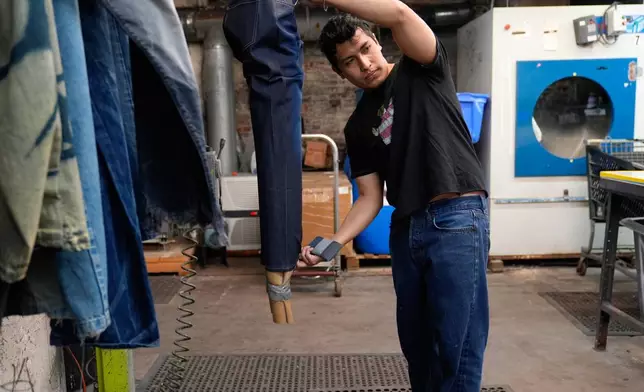 Bryan Morales Ibarra distresses denim by hand at the BPD Washhouse, a denim processing facility, in Jersey City, N.J., Tuesday, May 5, 2026. Behind him is a machine that uses ozone as part of the distressing process, as opposed to the traditional washing and chemicals. (AP Photo/Seth Wenig)