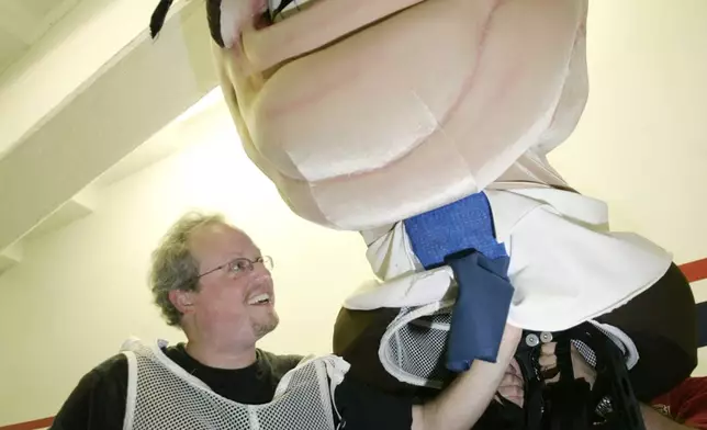 FILE- Associated Press Washington sports writer, Howard Fendrich, is helped with putting on the head piece representing President Teddy Roosevelt, before his participation in the fan favorite "President-Race", which is held in the middle of the fourth inning of the Washington Nationals baseball games, Aug. 17, 2006, at RFK Stadium in Washington. (AP Photo/Pablo Martinez Monsivais, File)