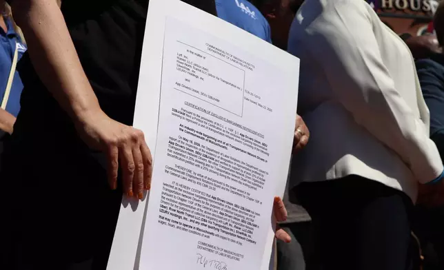 A demonstrator holds copy of a certification recognizing the App Drivers Union as the bargaining representative for Massachusetts rideshare drivers during a rally outside the Massachusetts State House after the App Drivers Union announced it had become the first certified union of rideshare drivers in the nation, on Tuesday, May 26, 2026, in Boston. (AP Photo/Leah Willingham)