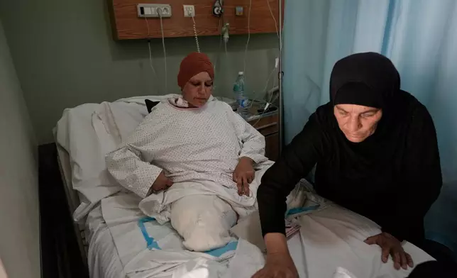 Sanaa Khalil, 35, a Syrian farmer who lost her two legs in the past days by an Israeli airstrike while she was working at a banana plantation, lies on a bed as she is assisted by a relative at a hospital in the southern port city of Tyre, Lebanon, Friday, May 1, 2026. (AP Photo/Hussein Malla)