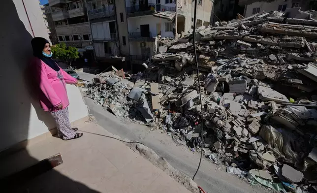 Em Ali Khodor, 75, looks through her damaged apartment into a destroyed building that was hit few weeks ago by an Israeli airstrikeafter she returns to the house, in the southern port city of Tyre, Lebanon, Thursday, April 30, 2026. (AP Photo/Hussein Malla)