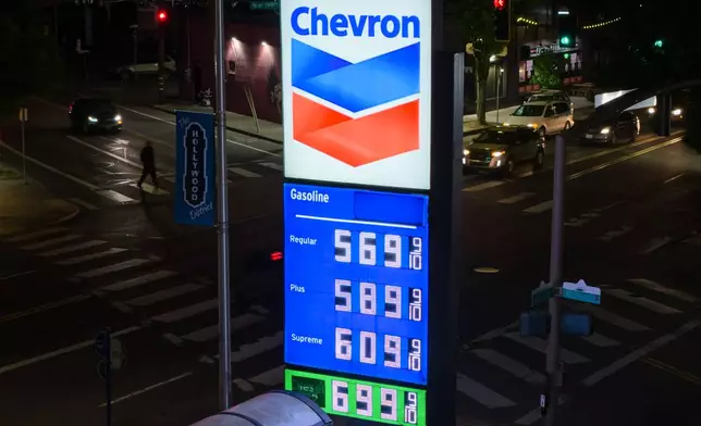 A person walks across the street as a sign for fuel prices is displayed at a gas station on Wednesday, May 6, 2026, in Portland, Ore. (AP Photo/Jenny Kane)