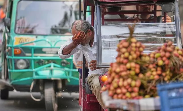 An electric rickshaw driver splashes water on his face to cool off under the intense summer heat in Lucknow, India, Wednesday, May 20, 2026. (AP Photo/Rajesh Kumar Singh)