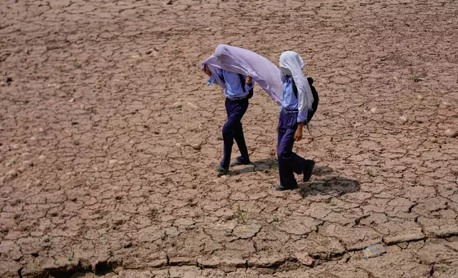 School children use cotton towels over their heads to protect themselves from the scorching afternoon heat as they walk through a parched field on the outskirts of Jammu, India, Wednesday, May 20, 2026. (AP Photo/Channi Anand)