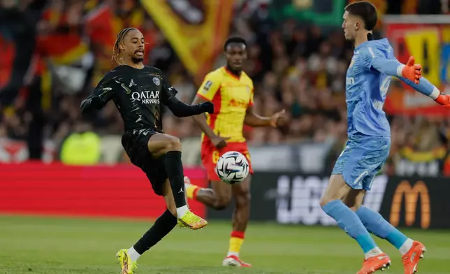 PSG's Bradley Barcola, left, kicks the ball towards Lens' goalkeeper Robin Risser during the French League One soccer match between Lens and Paris Saint Germain, in Lens, northern France, Wednesday, May 13, 2026. (AP Photo/Jean-Francois Badias)