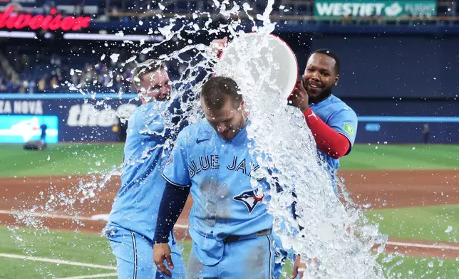 Toronto Blue Jays' Daulton Varsho is doused by Myles Straw (left) and Vladimir Guerrero Jr. after hitting a walk-off grand slam against the Tampa Bay Rays during 10th inning MLB baseball action in Toronto on Wednesday, May 13, 2026. (Nathan Denette/The Canadian Press via AP)