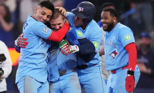 Toronto Blue Jays' Daulton Varsho (second left) celebrates his walk-off grand slam against the Tampa Bay Rays with Andres Gimenez (left) and George Springer during 10th inning MLB baseball action in Toronto on Wednesday, May 13, 2026. (Nathan Denette/The Canadian Press via AP)