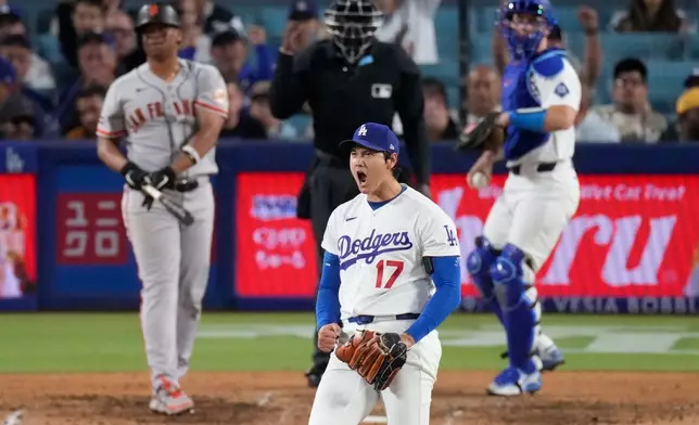 Los Angeles Dodgers two-way player Shohei Ohtani, center, reacts after striking out San Francisco Giants' Rafael Devers, left, as catcher Will Smith gets ready to throw the ball back during the sixth inning of a baseball game Wednesday, May 13, 2026, in Los Angeles. (AP Photo/Mark J. Terrill)