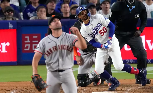 Los Angeles Dodgers' Mookie Betts, right, hits a solo home run as San Francisco Giants pitcher Robbie Ray, left, and catcher Jesus Rodriguez watch during the third inning of a baseball game Wednesday, May 13, 2026, in Los Angeles. (AP Photo/Mark J. Terrill)