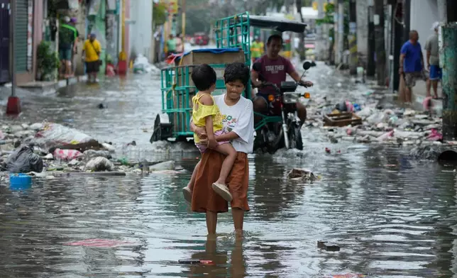 FILE - A woman and child crosses a flooded street due to Typhoon Fung-wong and high tide on Nov. 10, 2025, in Navotas, Philippines. (AP Photo/Aaron Favila, File)