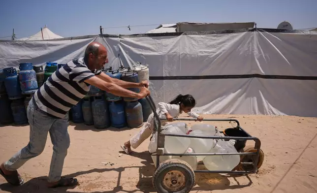 Ne'man Abu Jarad and his daughter push a cart loaded with jerrycans filled with water as they walk at a tent camp for displaced Palestinians in Khan Younis, southern Gaza Strip, Wednesday, May 13, 2026. (AP Photo/Abdel Kareem Hana)