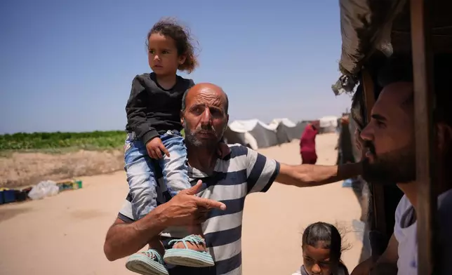 Ne'man Abu Jarad carries his granddaughter Hour Abu Jarad as he talks with a neighbor at a tent camp for displaced Palestinians in Khan Younis, southern Gaza Strip, Wednesday, May 13, 2026. (AP Photo/Abdel Kareem Hana)