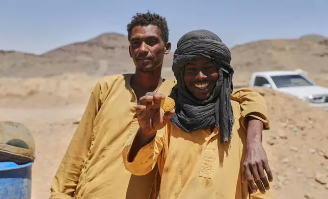 Miner Atta al-Khazin, right, shows a gold nugget produced by artisanal miners after processing ore at a mining site in Dalago Mahas, Sudan's Northern State, Friday, May 8, 2026.(AP Photo/Mohnd Blal)