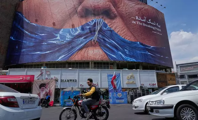 Vehicles drive past a billboard with graphic showing Strait of Hormuz and sewn lips of U.S. President Donald Trump in a square in downtown Tehran, Iran, Saturday, May 2, 2026. (AP Photo/Vahid Salemi)