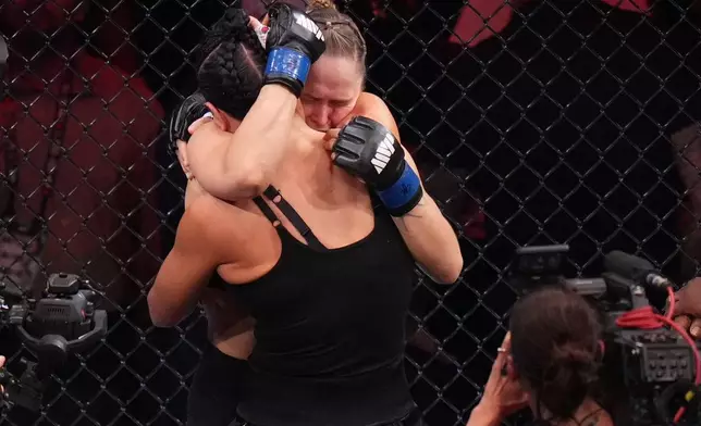 Ronda Rousey, of the United States, behind, hugs Gina Carano, of the United States, after defeating her in their featherweight mixed martial arts fight Saturday, May 16, 2026, in Inglewood, Calif. (AP Photo/Jae C. Hong )