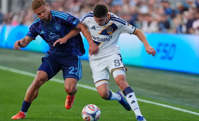 Sporting Kansas City midfielder Zorhan Bassong (22) and LA Galaxy midfielder Lucas Sanabria (8) battle for the ball during the first half of an MLS soccer match Wednesday, May 13, 2026, in Kansas City, Kan. (AP Photo/Charlie Riedel)