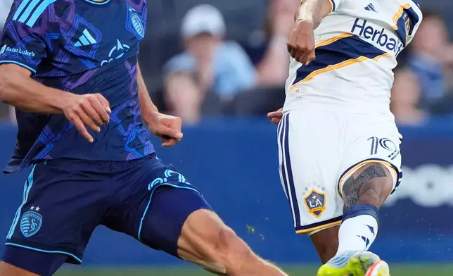LA Galaxy defender Mauricio Cuevas (19) kicks the ball past Sporting Kansas City midfielder Zorhan Bassong (22) during the first half of an MLS soccer match Wednesday, May 13, 2026, in Kansas City, Kan. (AP Photo/Charlie Riedel)
