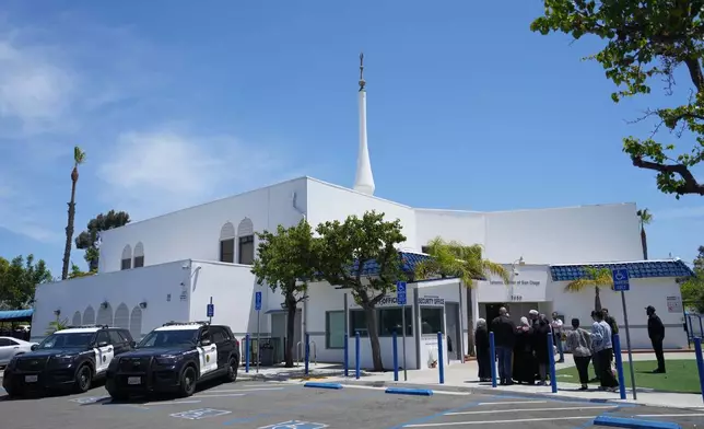 People gather as police vehicles are parked outside of the Islamic Center of San Diego, the day after a shooting, Tuesday, May 19, 2026, in San Diego. (AP Photo/Jae C. Hong)