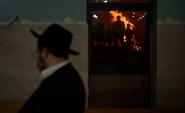 Ultra-Orthodox Jews are reflected in a window as they stand around a bonfire during Lag BaOmer, a holiday traditionally celebrated with bonfires, music, and gatherings, in Jerusalem, Monday, May 4, 2026. (AP Photo/Ohad Zwigenberg)